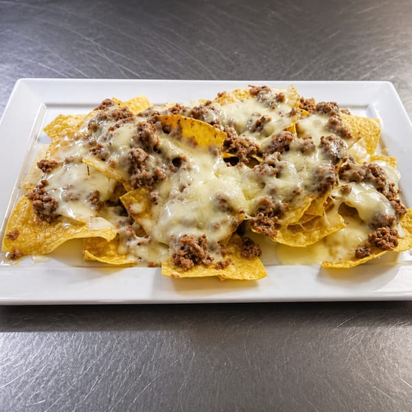 A white rectangular plate filled with golden tortilla chips, melted white cheese, and seasoned ground beef.