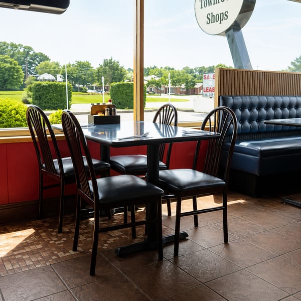 Diner interior with black tables and chairs, a blue booth, and large windows overlooking a green landscape.