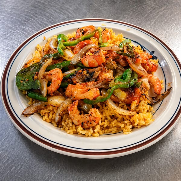 Shrimp fajitas with grilled onions and green peppers, served over yellow rice on a white plate.
