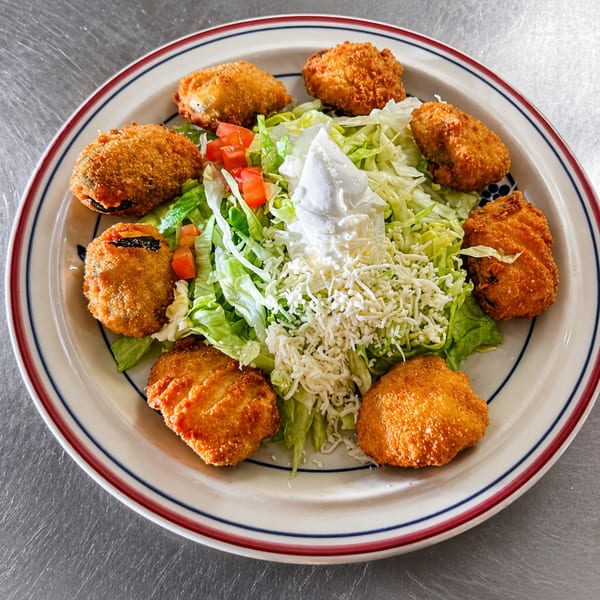 Eight golden-brown fried jalapeño poppers arranged around a bed of lettuce, tomatoes, and cheese.