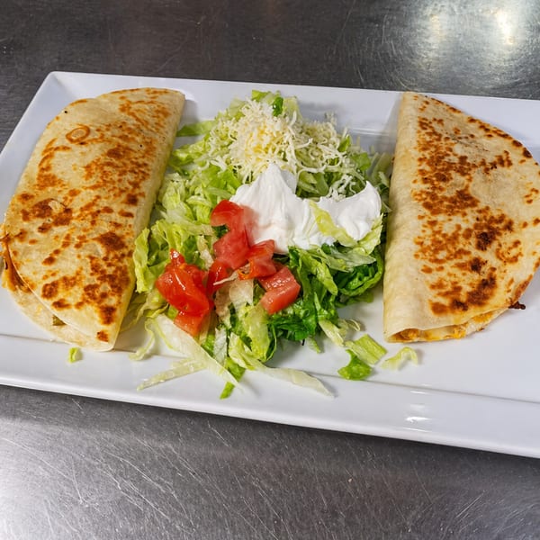 Two golden-brown quesadillas with a side of shredded lettuce, diced tomatoes, shredded cheese, and sour cream.
