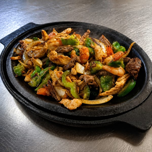 Sizzling fajitas with chicken, beef, shrimp, onions, and green bell peppers in a black skillet.